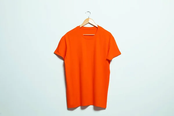 Hanger with orange t-shirt on light wall. Mockup for design