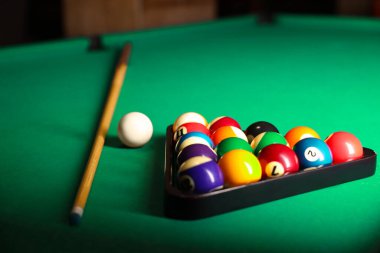Plastic triangle rack with billiard balls and cue on green table, closeup