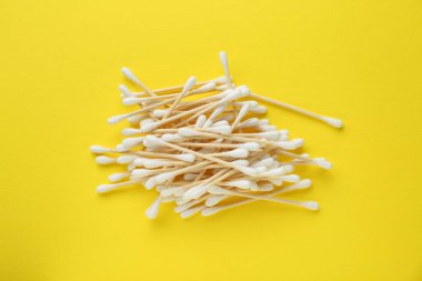 Heap of wooden cotton buds on yellow background, flat lay