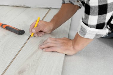 Yeni kaplama döşeme kurulumu sırasında kalem kullanan profesyonel bir işçi.