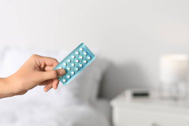 Woman holding blister of oral contraception pills against blurred background, closeup. Space for text