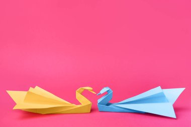 Paper swans on pink background, space for text. Origami art