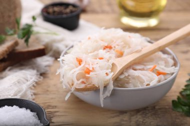 Bowl of tasty sauerkraut and ingredients on wooden table, closeup