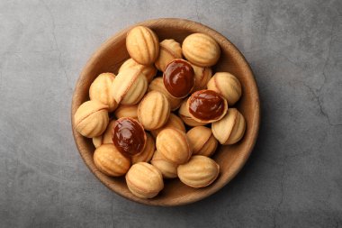 Delicious nut shaped cookies with boiled condensed milk in wooden bowl on gray textured table, top view