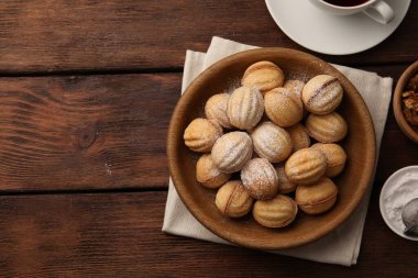 Delicious nut shaped cookies with boiled condensed milk and powdered sugar on wooden table, flat lay. Space for text