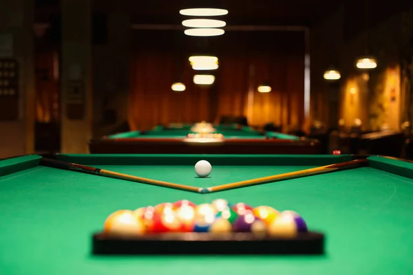 Plastic triangle rack with billiard balls and cues on green table indoors, selective focus