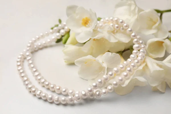Beautiful pearl necklace and flowers on white marble table, closeup