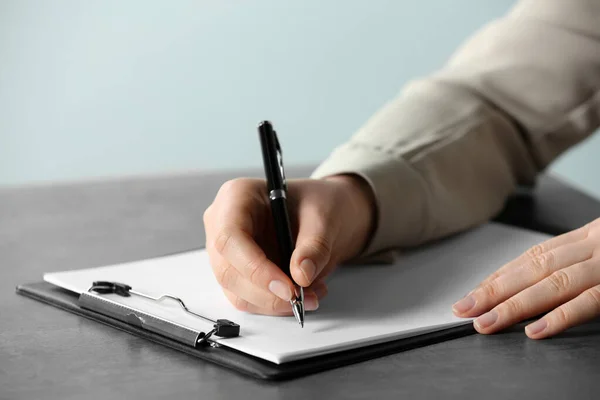 Woman writing in documents with pen at grey table, closeup