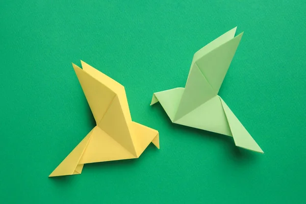 Beautiful colorful origami birds on green background, flat lay