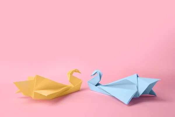 Origami art. Beautiful paper swans on pink background