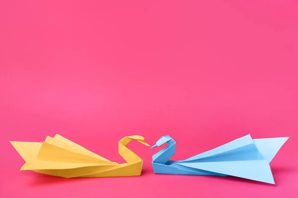 Paper swans on pink background, space for text. Origami art