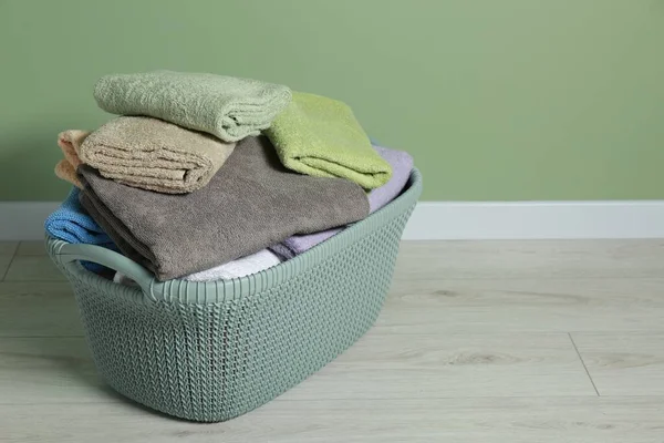Plastic laundry basket with clean terry towels on floor near light green wall. Space for text