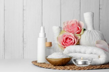 Composition with different spa products, candle and roses on white table against wooden background. Space for text