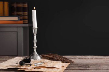 Inkwell, feather, fountain pen, candlestick and vintage parchment with ink stains on wooden table indoors. Space for text
