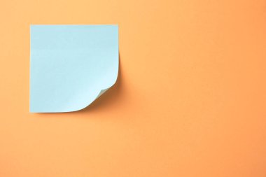 Blank paper note on pale orange background, top view. Space for text
