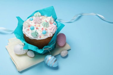 Traditional Easter cake with meringues and painted eggs on light blue background, space for text