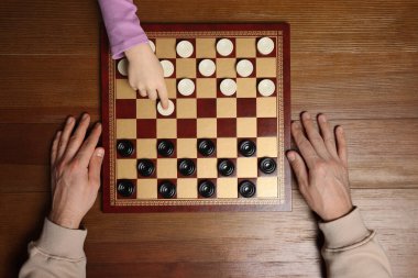 Man playing checkers with child at wooden table, top view