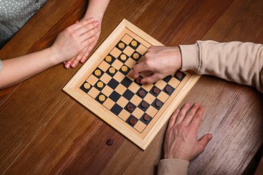 Man playing checkers with woman at wooden table, above view