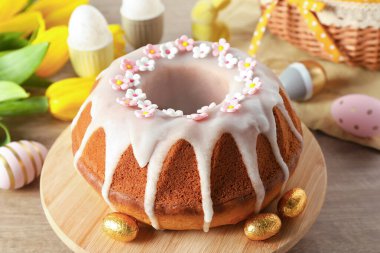 Delicious Easter cake decorated with sprinkles near painted eggs and tulips on wooden table, closeup