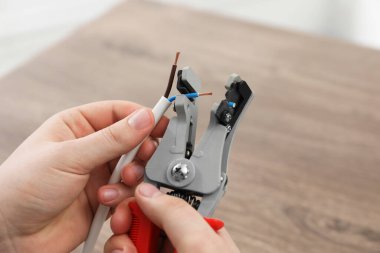 Professional electrician stripping wiring at wooden table, closeup