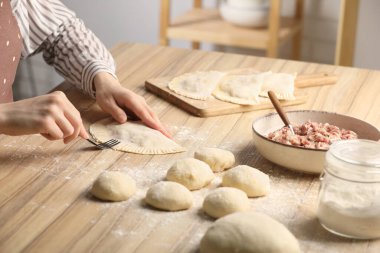 Woman making chebureki at wooden table indoors, closeup