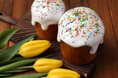 Tasty Easter cakes and flowers on wooden table