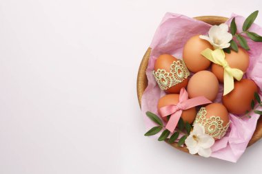Easter eggs with colorful bows, twigs and flowers on white background, top view. Space for text