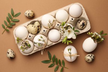 Festive composition with eggs and floral decor on brown background, flat lay. Happy Easter