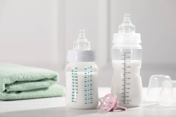 Feeding bottles with milk, pacifier and towel on white wooden table
