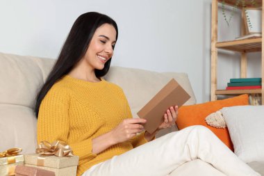 Happy woman reading greeting card on sofa in living room