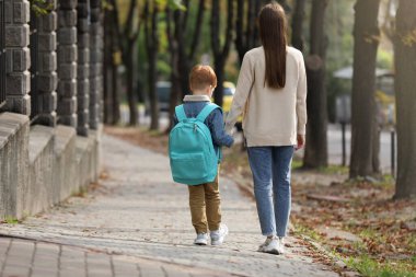 Young mom taking her son to school, back view