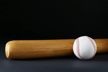 Wooden baseball bat and ball on black background, space for text. Sports equipment