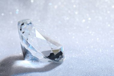 Beautiful dazzling diamond on white glitter fabric, closeup. Space for text