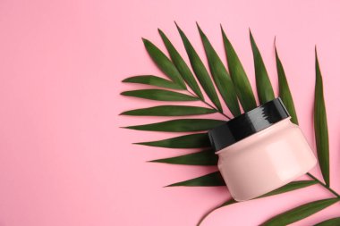 Jar of cream and palm leaf on pink background, top view. Space for text