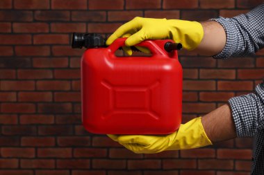 Man holding red canister against brick wall, closeup