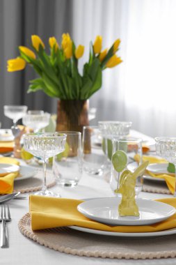 Festive table setting with glasses, painted eggs and vase of tulips. Easter celebration