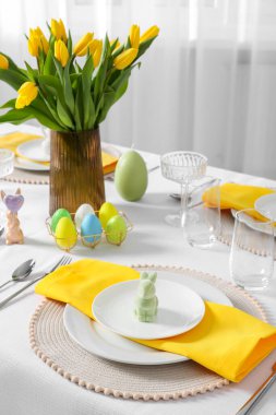 Festive table setting with glasses, painted eggs and vase of tulips. Easter celebration