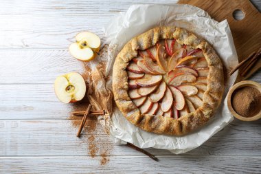 Delicious apple galette and cinnamon on white wooden table, flat lay