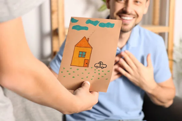 Happy man receiving greeting card from his son at home, closeup