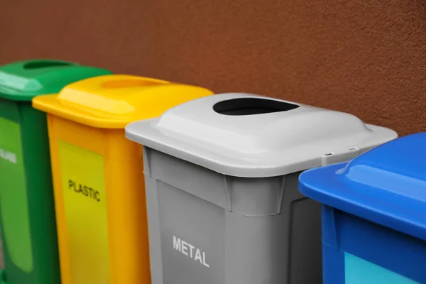 Many color recycling bins near brown wall, closeup