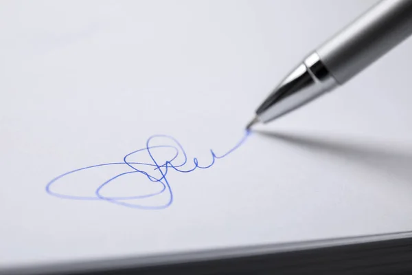Signing on sheet of white paper with pen, closeup
