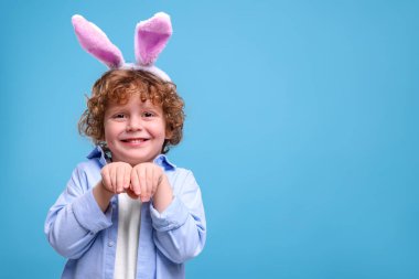 Portrait of happy boy wearing bunny ears headband on light blue background. Space for text. Easter celebration