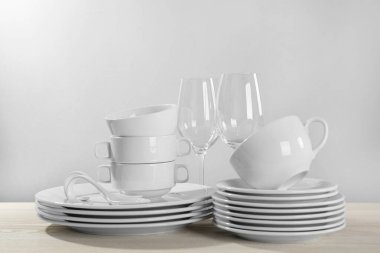 Set of clean dishware and glasses on white wooden table against light background