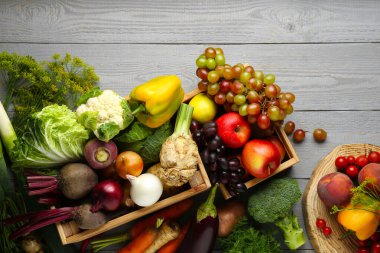 Different fresh vegetables and fruits in crates on grey wooden table, flat lay. Farmer harvesting