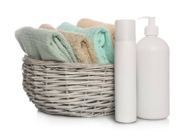 Soft towels in wicker basket and bottles of cosmetic products on white background