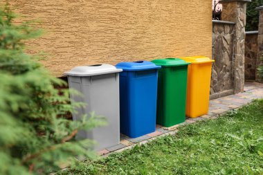 Many colorful recycling bins near yellow wall outdoors