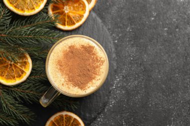 Glass cup of delicious eggnog with cinnamon and dried orange slices on gray table, flat lay. Space for text