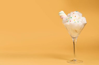 Martini glass with cotton, sprinkles and marshmallow on yellow background. Space for text