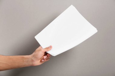 Man holding sheets of paper on grey background, closeup. Mockup for design