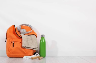 Backpack and sports equipment on floor near white wall, space for text